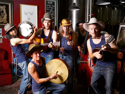 The Pigs - Sechs Musiker stehen in einer Bar. Sie tragen alle blaue Unterhemden, Jeans und Western-Hüte.