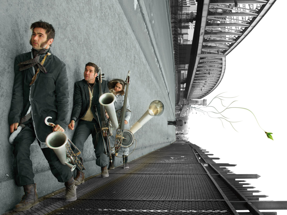 Drei Personen laufen über eine Brücke. Sie tragen graue Anzüge und selbst gebaute Instrumente. Etwas sieht falsch aus, die Brücke liegt auf der Seite.